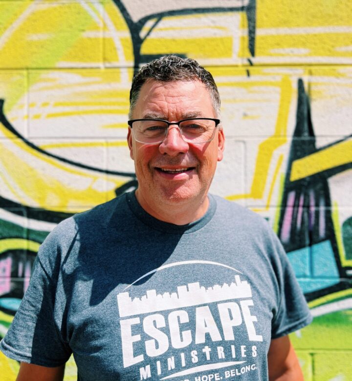Man smiling in front of a colorful graffiti wall.