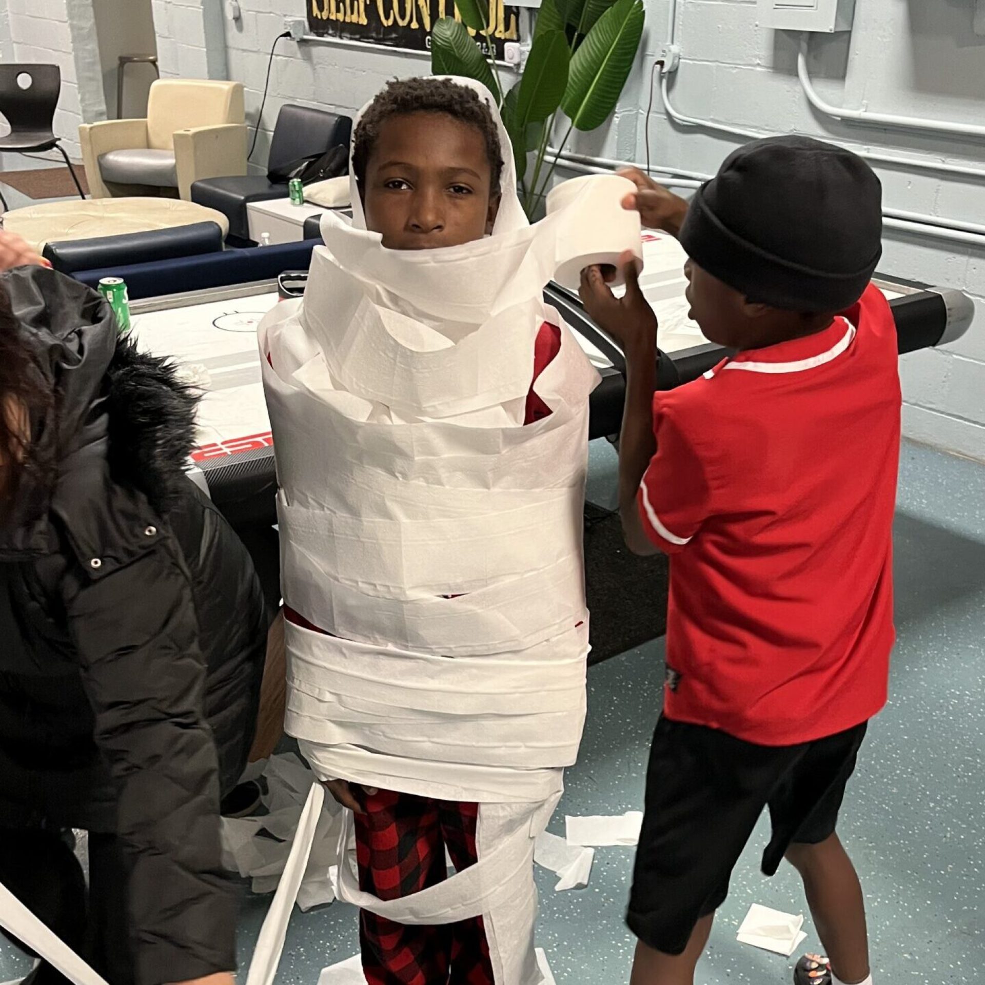 Children wrapping a friend in toilet paper for a fun activity indoors.