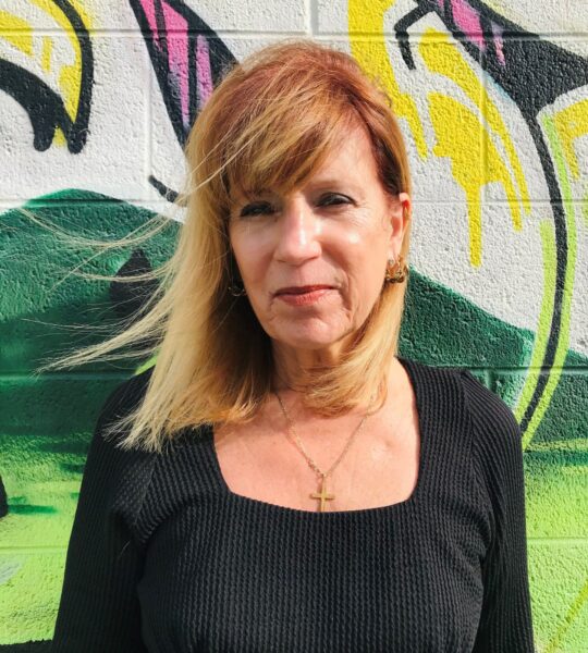 Woman with blonde hair stands against a colorful graffiti wall.