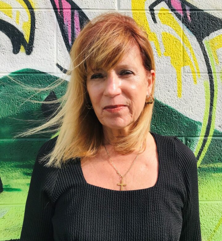 Woman with blonde hair stands against a colorful graffiti wall.