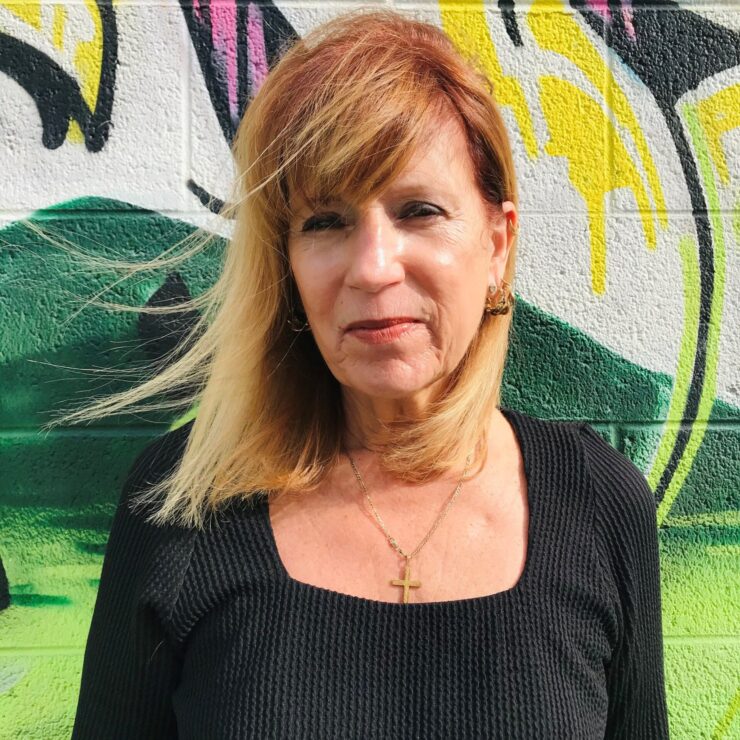 Woman with blonde hair stands against a colorful graffiti wall.