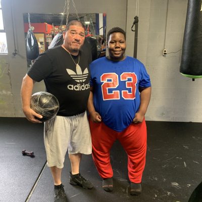 Two men posing in a gym, one holding a basketball.
